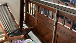 A balcony with a wooden railing, a chair, a table with a cup of coffee, a potted plant, and a magazine.