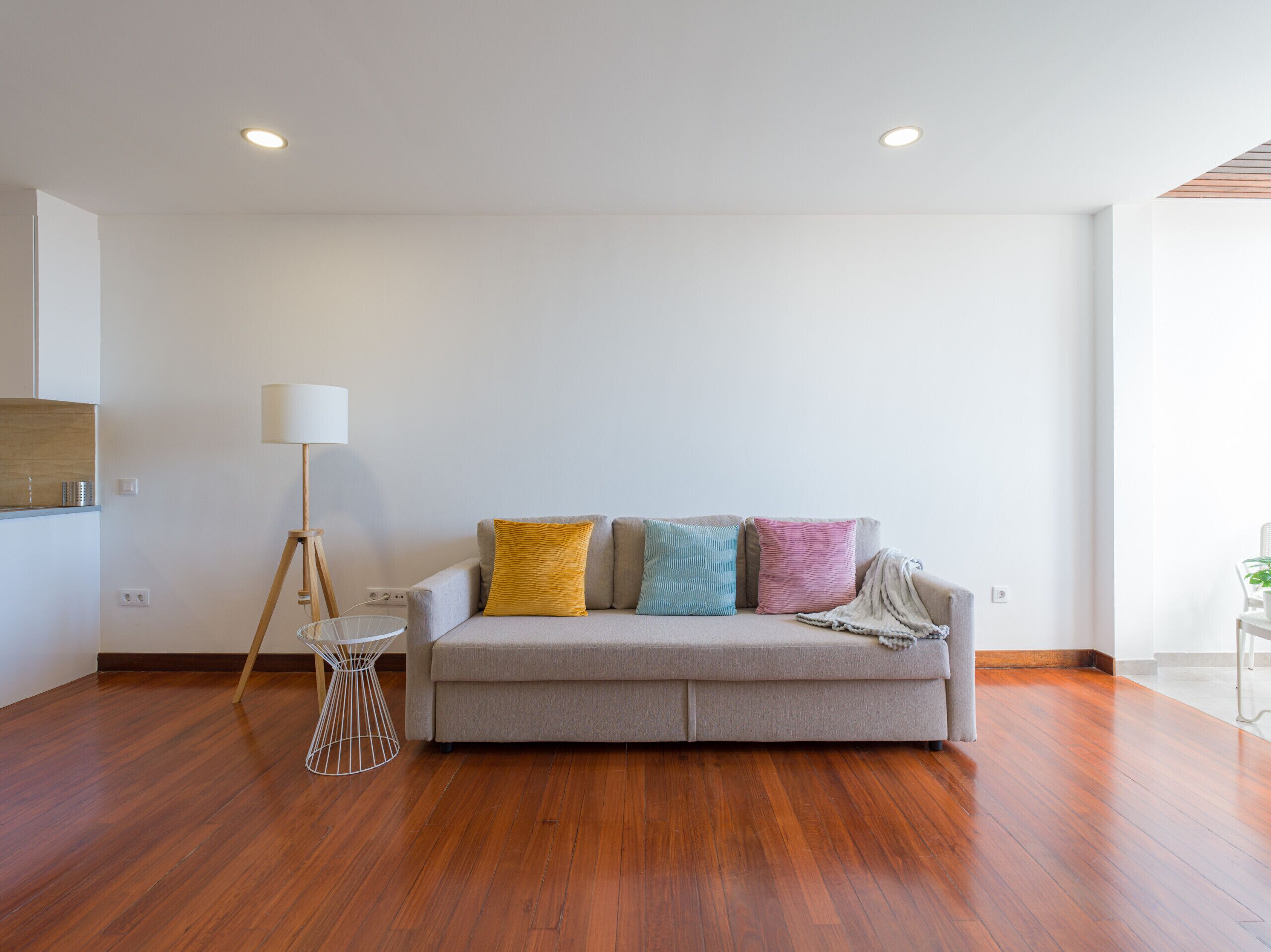 Una sala de estar moderna con un sofá gris, cojines coloridos, una lámpara de pie y suelo de madera.
