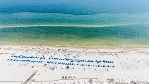 A beach with rows of blue umbrellas and lounge chairs, a clear view of the ocean, and a sandy shoreline. - Gulf Front - 3BR 4BA - Lazy River - The Oasis at Orange Beach (Orange Beach)