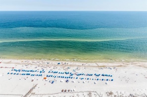A beach with rows of blue umbrellas and lounge chairs, a clear view of the ocean, and a sandy shoreline. - Gulf Front - 3BR 4BA - Lazy River - The Oasis at Orange Beach (Orange Beach)