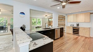 A modern kitchen with a granite countertop, stainless steel appliances, and wooden cabinets. - Salty Sea Life - Canal Pool Home-Just 5 Min to Anna Maria Island - By Island Rea (Bradenton)