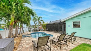 A backyard with a swimming pool, palm trees, and outdoor furniture. - Salty Sea Life - Canal Pool Home-Just 5 Min to Anna Maria Island - By Island Rea (Bradenton)