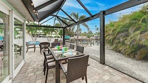 An outdoor patio with a table set for dining, surrounded by wicker chairs, and overlooking a pool area with palm trees. - Salty Sea Life - Canal Pool Home-Just 5 Min to Anna Maria Island - By Island Rea (Bradenton)