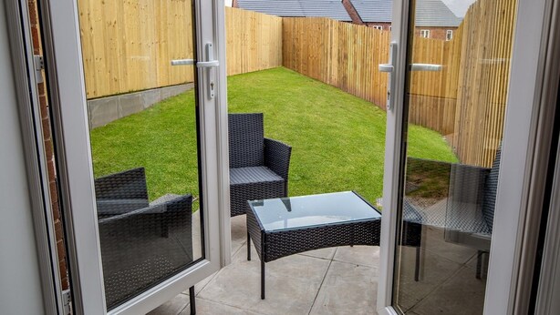 A patio with a glass door, a grassy lawn, and a wooden fence. - Modern and bright 2-bed home near Ludlow centre - Pass the Keys (Ludlow)