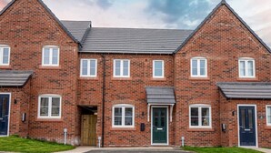 A two-story brick building with a symmetrical facade, featuring evenly spaced windows and doors, a central entrance with a green door, and a gravel driveway. - Modern and bright 2-bed home near Ludlow centre - Pass the Keys (Ludlow)