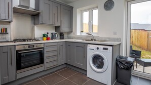 A modern kitchen with grey cabinets, a built-in oven, a washing machine, and a window overlooking a backyard. - Modern and bright 2-bed home near Ludlow centre - Pass the Keys (Ludlow)