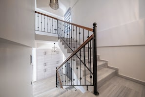Un escalier avec une main courante en bois et des balustres noires, menant à un palier où se trouve un luminaire.