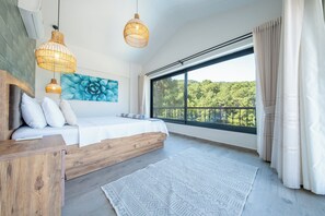 A modern bedroom with a large window, a bed with white bedding, a wooden headboard, and a geometric patterned rug.