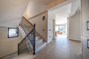 A spacious interior with a staircase leading to a balcony, a large window, and a view of the outdoors.