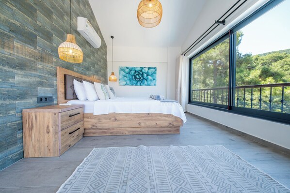 A modern bedroom with a large window, a wooden bed, and a geometric-patterned rug.