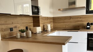 Una cocina moderna con encimera de madera, dos taburetes, un microondas, un hervidor y una cafetera.