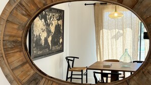 Un espejo redondo con marco de madera que refleja un comedor con una mesa, sillas, una lámpara colgante y un mapa mundial enmarcado en la pared.