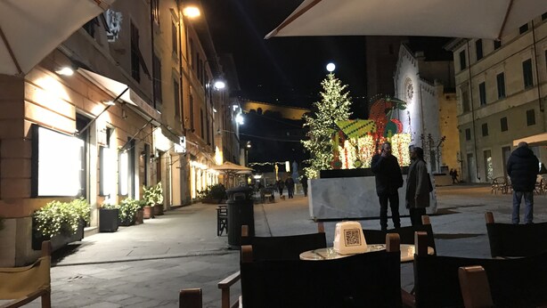 An outdoor seating area with tables and chairs, a decorative tree, and a building with illuminated windows in the background. - Loft Angela Charming Aptmnt in Pietrasanta Center (Pietrasanta)