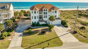 Una propiedad frente a la playa de varios pisos con un edificio central grande, un porche cubierto y un césped bien cuidado.