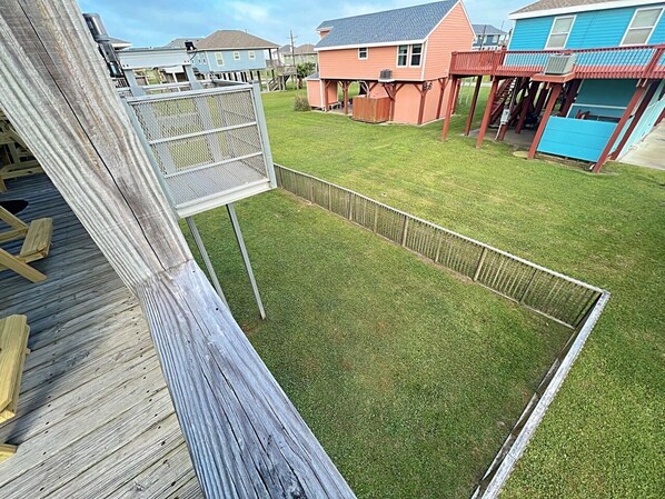 A backyard with a wooden deck, a fenced play area, and a house with a blue exterior.