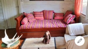 Ein gemütliches Zimmer mit einer Holzsofa, verziert mit bunten, gestreiften Kissen, einer kleinen Hundestatue und einem dekorativen Geweih auf einer gewebten Matte.
