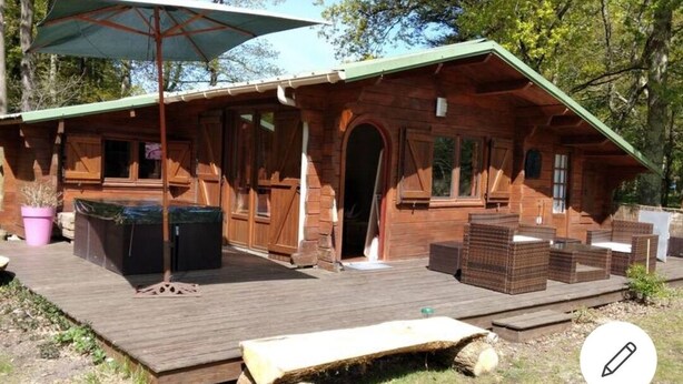 Eine Holzhütte mit grüner Dachdeckung, einer Veranda und Sitzgelegenheiten im Freien.