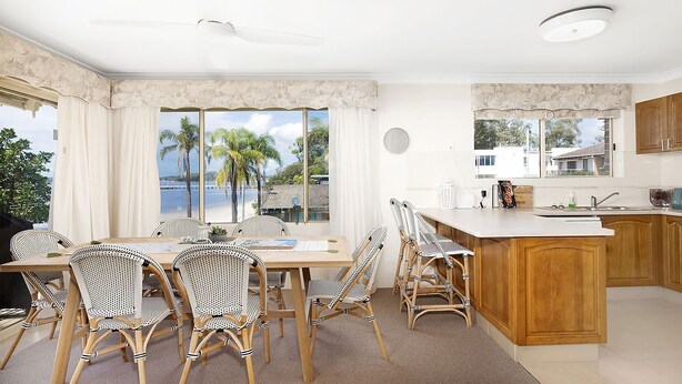 A modern kitchen with a large island, wooden cabinets, and a view of palm trees and a beach. - Soldiers Point Absolute Waterfront The Peninsula (Soldiers Point)