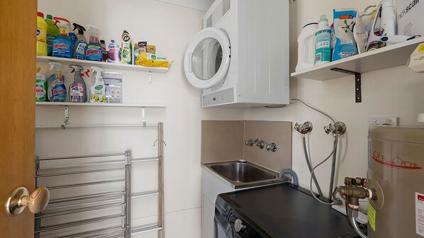 A laundry room with a washing machine, shelves with cleaning products, a sink, and a towel rack. - Soldiers Point Absolute Waterfront The Peninsula (Soldiers Point)