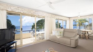 A spacious living room with a large TV, a beige sofa, and a dining area with a table and chairs. - Soldiers Point Absolute Waterfront The Peninsula (Soldiers Point)