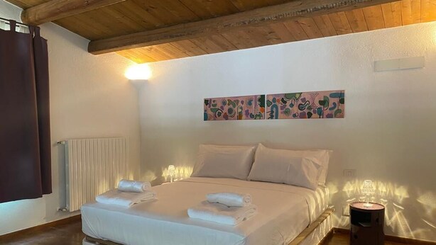 Un dormitorio con techo de madera, una cama con ropa blanca, un radiador y una lámpara fijada en la pared.