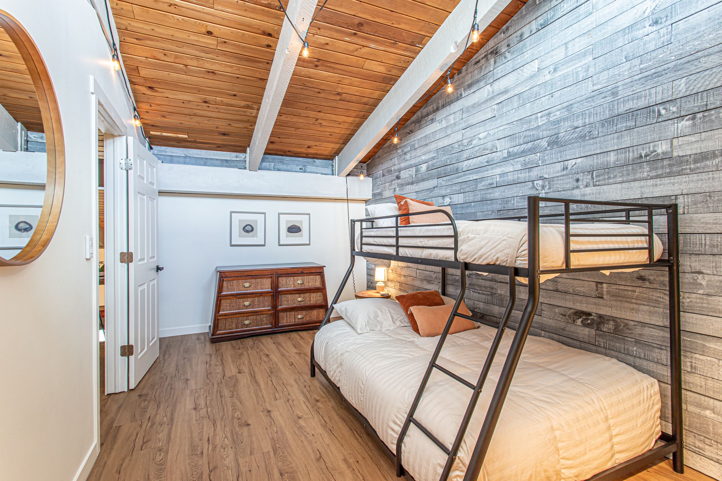A bunk bed room with wooden flooring, a rustic wall, and a ceiling with exposed beams.