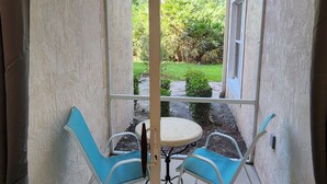 Eine Glastür führt zu einer Terrasse mit einem runden Tisch und zwei blauen Stühlen.