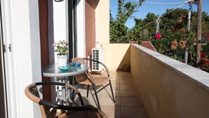 A balcony with a table and chairs, a potted plant, and a view of a garden with trees and flowers.