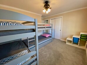 A bunk bed room with a ceiling fan, a door, and storage shelves.