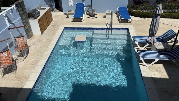 A rectangular swimming pool with clear blue water, surrounded by lounge chairs and umbrellas.