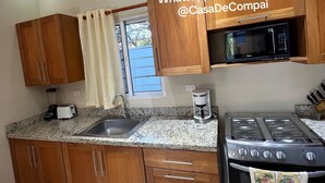 A kitchen with wooden cabinets, a granite countertop, a sink, a microwave, a stove, and a window with curtains.