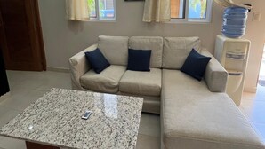 A living room with a beige sectional sofa, a marble coffee table, and a water dispenser.