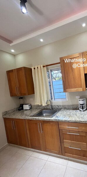 Una cocina con armarios de madera, encimera de granito, pileta, microondas, estufa y ventana con cortinas.