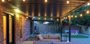 A covered patio area with a wooden ceiling, string lights, a beige sofa, and a colorful game board. - Rancho de Valle del Norte - An Irvie Home (Albuquerque)