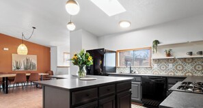 Una cocina moderna con una isla central, un comedor con mesa y sillas, y un gran ventanal.