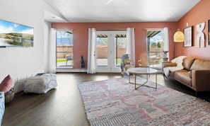 A spacious living room with a large window, a brown leather sofa, a patterned rug, and a dining area with a table and chairs. - Rancho de Valle del Norte - An Irvie Home (Albuquerque)