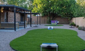 A backyard with a lawn, a ping pong table, a covered seating area, and a colorful play structure. - Rancho de Valle del Norte - An Irvie Home (Albuquerque)