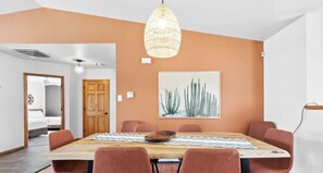 A dining area with a wooden table, red chairs, a hanging light fixture, and a cactus artwork on the wall. - Rancho de Valle del Norte - An Irvie Home (Albuquerque)
