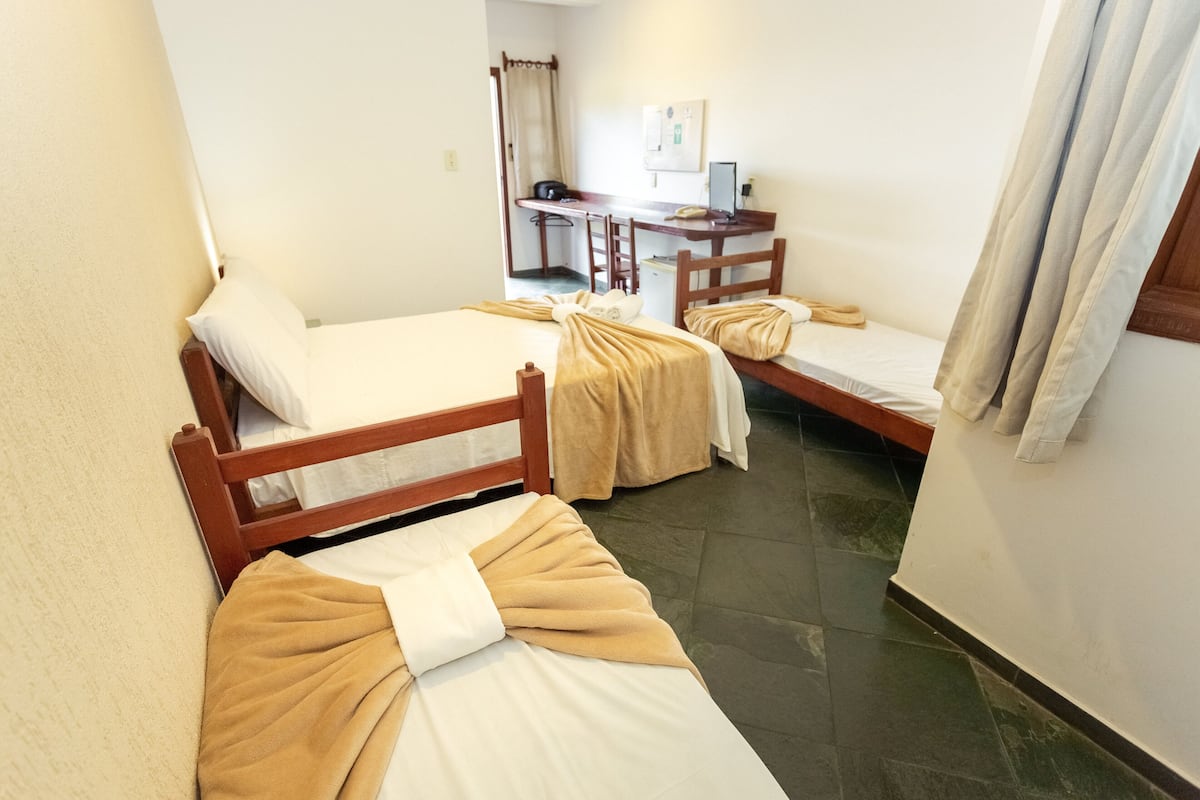 Ein kleines, kompaktes Hotelzimmer mit zwei Einzelbetten, einem Schreibtisch mit Stuhl und einer kleinen Küchenzeile.