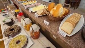 A buffet counter with various food items including bread, pastries, and condiments. - Pousada Céu de Estrelas (Bonito)