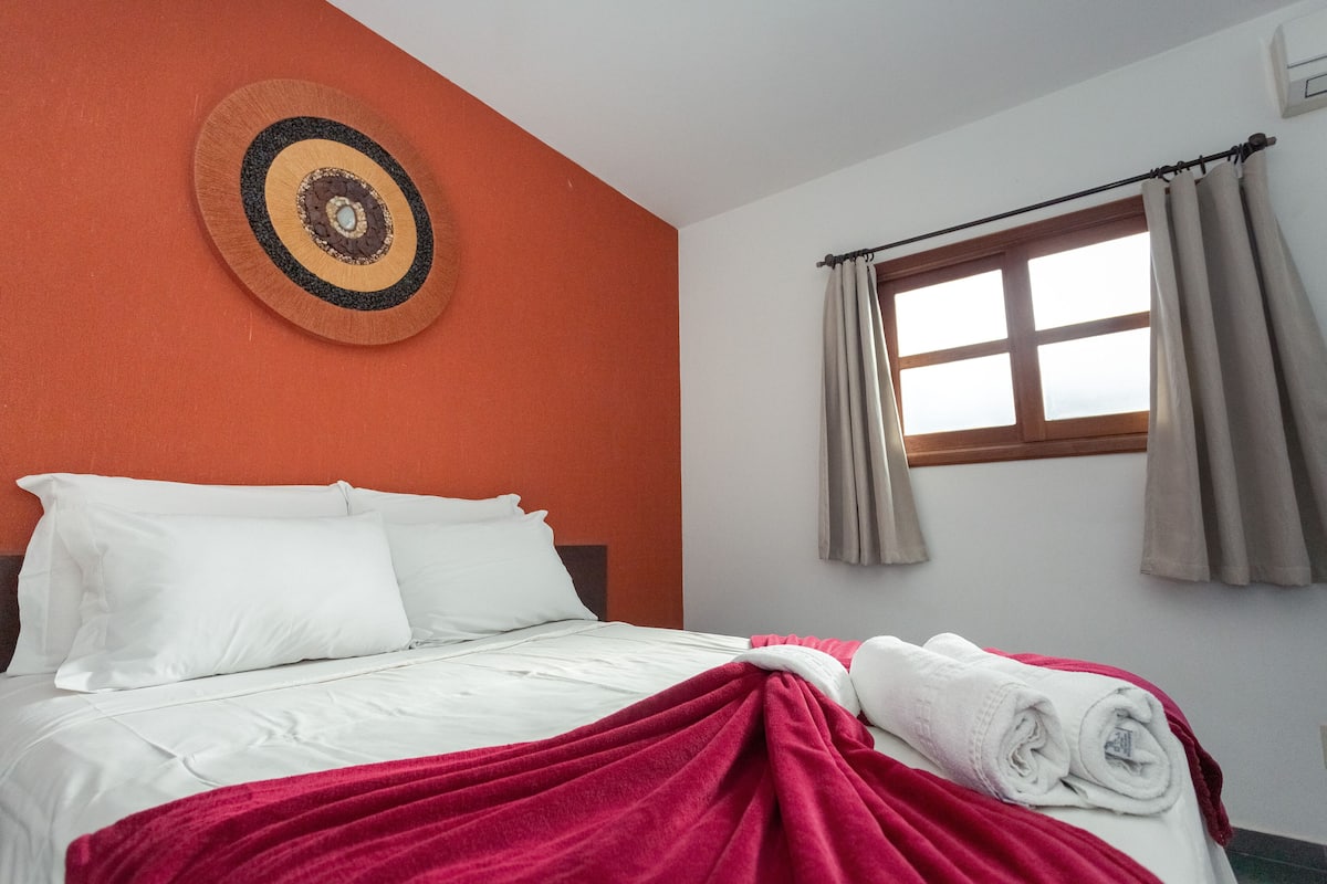 Ein Hotelzimmer mit Bett, weißer Bettwäsche, einer roten Decke, einem Fenster mit Vorhängen und einer Wanddekoration.