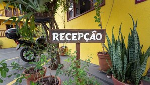 A sign reading "RECEPCAO" in front of a yellow building with potted plants and a motorcycle parked nearby. - Pousada Céu de Estrelas (Bonito)