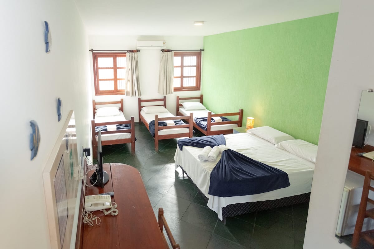 Ein Schlafsaalzimmer mit vier Einzelbetten, einem Schreibtisch mit Telefon und einer Wand in Grüntönen.