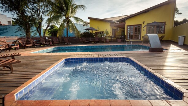 A pool area with two hot tubs, lounge chairs, and a yellow building. - Pousada Céu de Estrelas (Bonito)