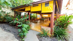 A covered outdoor patio with wooden furniture and a concrete pathway. - Pousada Céu de Estrelas (Bonito)