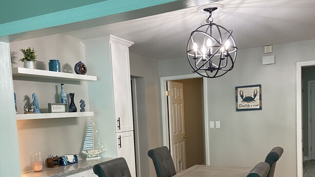 A dining area with a wooden table and chairs, white cabinets, and a decorative ceiling light.