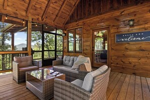 Una baita di legno con mobili in vimini, ampie finestre e un cartello con la scritta 'Hello and Welcome'.