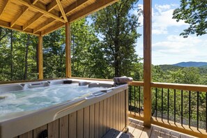 A hot tub on a wooden deck with a view of a forest and mountains.
