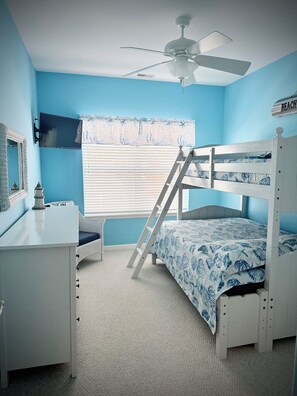 A bedroom with a bunk bed, a desk, a chair, a ceiling fan, and a window with blinds.
