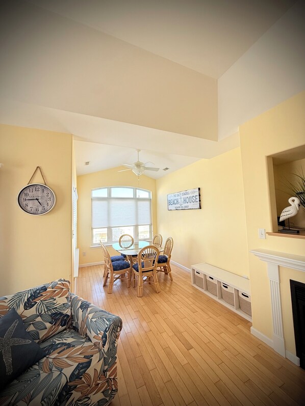 A dining area with a round table and chairs, a clock on the wall, and a fireplace.